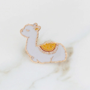 Close-up of a cute white enamel alpaca brooch with golden outlines and orange patterns