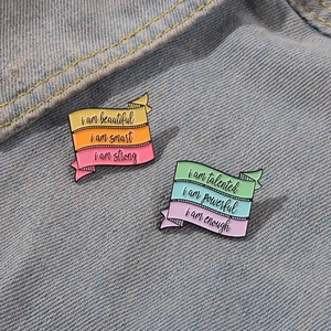 Set of two colorful striped enamel pins with motivational quotes on denim background