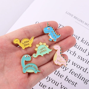 Gros plan de cinq pins en émail colorés avec des dinosaures tenus dans une main
