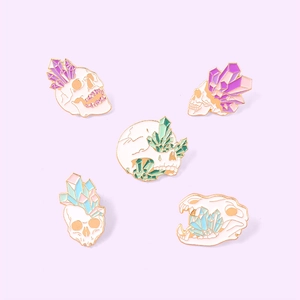 Detailed macro view of five macaron colored crystal skull enamel pins with gold plating