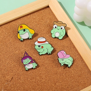 Détail de cinq broches assorties en émail de grenouilles sur un tableau en liège