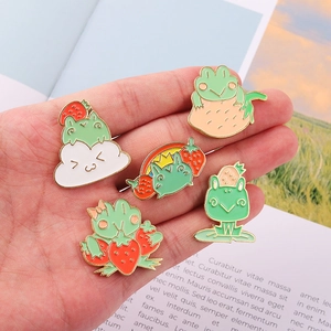 Close-up of five cute strawberry frog enamel pins held in hand to show size and detail