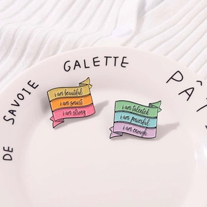 Colorful enamel scroll banner pins with motivational phrases on a ceramic plate