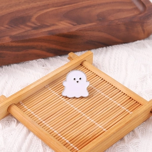 Macro detail of a white ghost enamel pin with silver outlines on a soft knit background