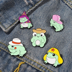 Set of five funny enamel frog pins with colorful wizard and cowboy hats on denim fabric