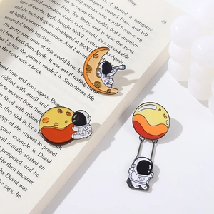 Lot de pins émaillés astronaute avec motifs lune et planète présentés sur un livre ouvert