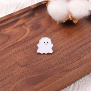 Cute white ghost enamel brooch on a warm wooden tray with textured background