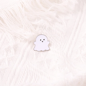 Cute white ghost enamel pin with silver metal edges on a white knitted texture background