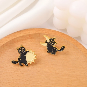 Close-up of black cat enamel pins with gold sun and moon motifs on a white fabric background