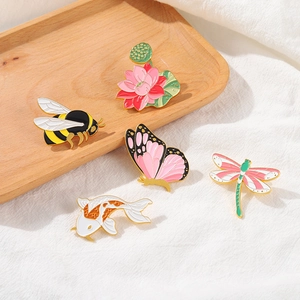 Cinq broches en émail aux motifs d'animaux et de fleurs, abeille et papillon sur plateau bois