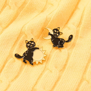Detailed view of two black cat enamel pins featuring golden sun and moon designs