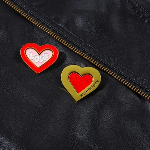 Detailed close-up of pink LOVE and golden serendipity heart enamel pins on leather