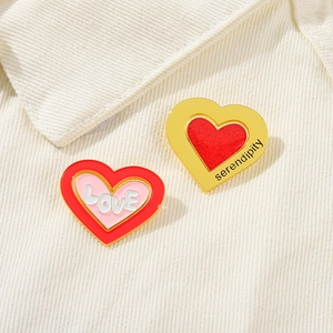 Macro shot of heart-shaped enamel pins with LOVE and serendipity text on corduroy