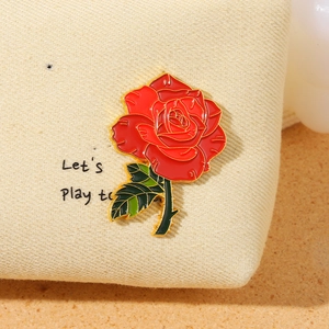 Spilla fiore rosa rossa smaltata con bordo dorato e foglie verdi su tessuto beige