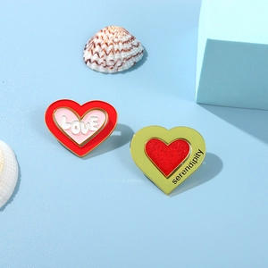 Detail of pink and green heart enamel pins with LOVE and serendipity text on blue background