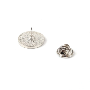 Macro shot of silver circular brooch back with textured finish and butterfly clasp attachment