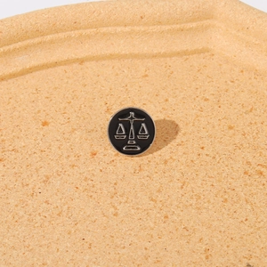 Macro detail of round Libra zodiac enamel pin with silver scales on black background