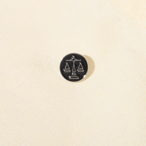 Minimalist black enamel Libra scales brooch pin in silver metal on textured fabric