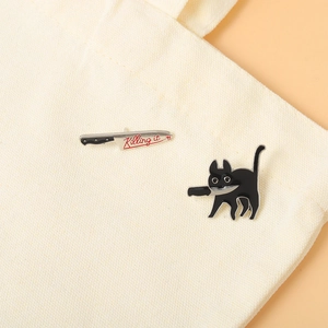 Detail of black cat enamel pin and knife badge with Killing it text on a canvas bag