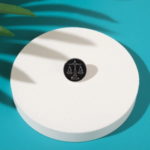 Macro view of Libra zodiac enamel pin in black and silver on a white pedestal