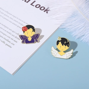 Detail view of cartoon enamel brooches with purple butterfly and white angel wings on blue background