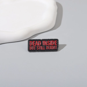 Detail of a rectangular enamel pin featuring red text on a black metal background
