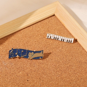 Music themed enamel pins featuring a piano keyboard and a cat on a starry staff