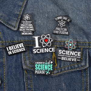Set of six enamel science badges with atoms and lab gear on a denim jacket pocket