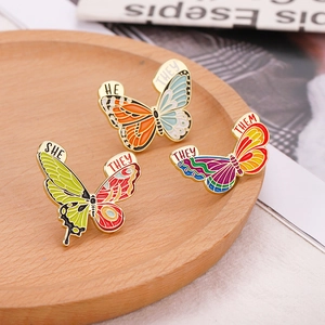 Vue détaillée des broches papillon émaillées avec pronoms SHE THEY HE THEM sur bois