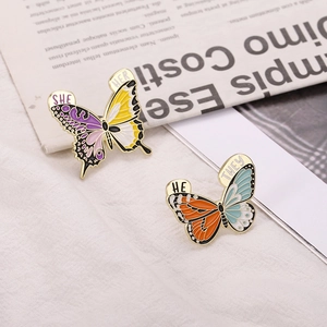 Détail de broches papillon émaillées colorées avec les pronoms SHE/HER et HE/THEY