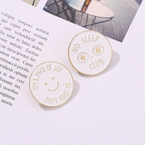Detail of two white enamel pins with gold edges featuring minimalist slogans on a magazine background