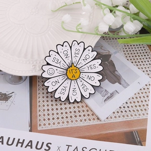 Creative rotating daisy enamel brooch with Yes and No petals on a white ceramic plate