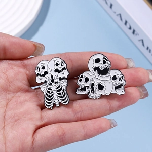 Close-up of hand holding two punk skull enamel pins with black and white finish