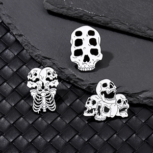 Detailed macro view of three gothic skull enamel pins on textured black leather and rock surface
