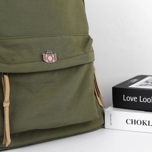 Detail of cute black cat enamel pin on a dark green canvas bag with leather drawstring