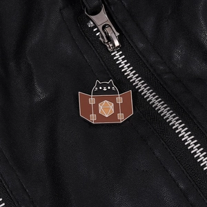 Detail of cute black cat enamel pin with D20 dice design on a black leather jacket