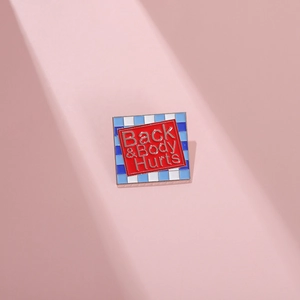 Macro shot of rectangular enamel pin with Back & Body Hurts text on pink surface