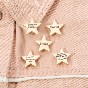 Set of five star-shaped enamel pins with motivational quotes on pink denim fabric