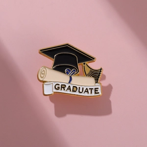 Enamel graduation pin with black mortarboard and white Graduate banner on pink surface