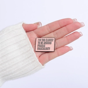 Pink enamel brooch featuring I'm too clumsy to be around fragile masculinity slogan
