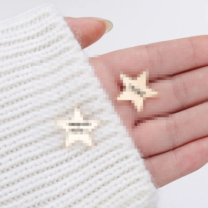 Star shaped golden alloy brooches with letter engraving on white knitted fabric