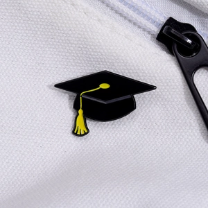 Close-up of black graduation cap enamel pin with yellow tassel on white canvas bag
