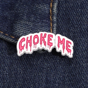 Detailed view of Choke Me enamel pin with pink dripping letters on denim fabric