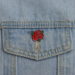 Detail of a red enamel rose brooch with green leaves pinned on blue denim fabric