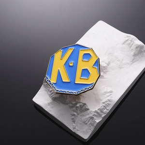 Creative octagonal K-B enamel pin in bright blue and yellow on white textured stone base