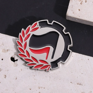 Round metal enamel pin badge featuring red and black flags with laurel leaf design