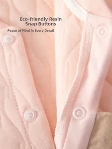 Gros plan des boutons-pression en résine sur le tissu matelassé rose de la barboteuse