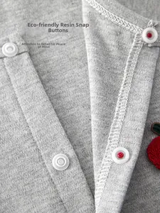 Detail of eco-friendly resin snap buttons and red apple embroidery on grey baby romper