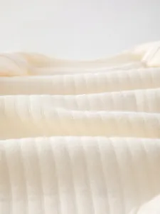 Macro detail of soft ribbed cotton fabric on a newborn winter romper in beige color