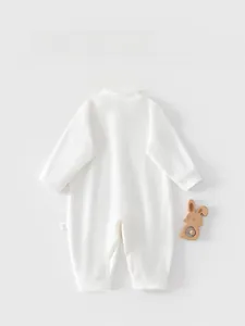 Detail view of the back of a white long-sleeve cotton baby romper with a wooden rattle